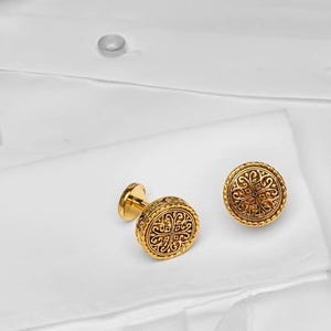 May include: A pair of gold cufflinks with an intricate floral design.