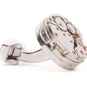 May include: Silver cufflinks with a round, exposed watch mechanism. The cufflinks are made of polished metal and have a classic design.