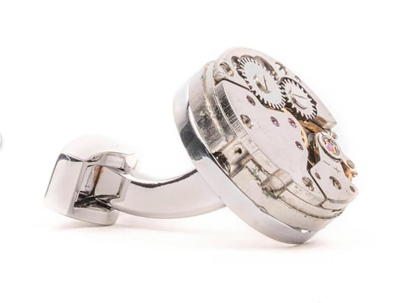 May include: Silver cufflinks with a round, exposed watch mechanism. The cufflinks are made of polished metal and have a classic design.