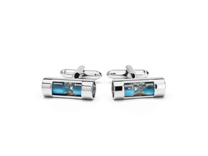 May include: A pair of silver-toned cufflinks featuring a cylindrical design with a clear glass center. Inside each cylinder is a miniature hourglass filled with bright blue sand, visible through the transparent casing and polished metal frame.