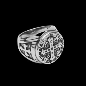 May include: A silver ring with a round, black, detailed design featuring a cross and the words "S.P.D.  ND.S.M.D.  C.S.S.M.D.  P.L.  V.B.  PAX  VBS".