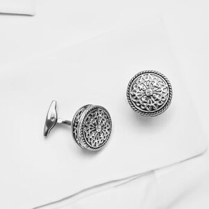 K&ouml;nnte beinhalten: Ein Paar silberne Manschettenkn&ouml;pfe mit komplizierten kreisf&ouml;rmigen Designs.