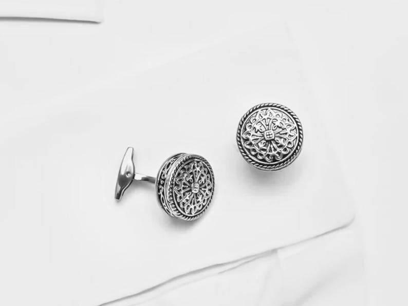 K&ouml;nnte beinhalten: Ein Paar silberne Manschettenkn&ouml;pfe mit komplizierten kreisf&ouml;rmigen Designs.