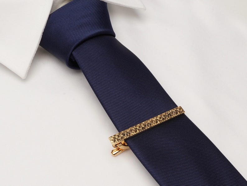 May include: A navy blue tie with a gold tie clip. The tie clip has a textured design.