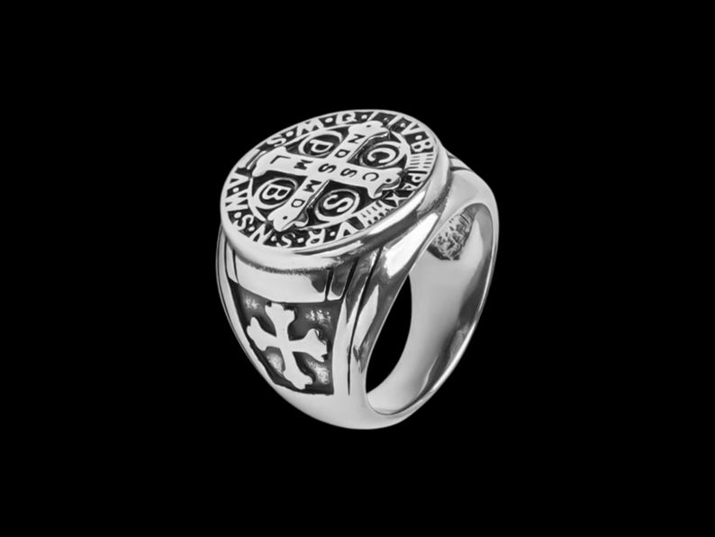 May include: A silver ring with a detailed design featuring a cross and the words "S.P.Q.R." and "INRI".