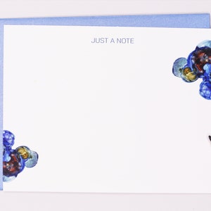 Può includere: Set di cancelleria bianco con busta blu e matita. Il biglietto da visita riporta la scritta "JUST A NOTE" in blu. Disegni astratti ad acquerello blu e rossi sono negli angoli del biglietto.