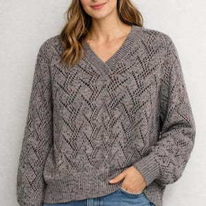 May include: A gray, open-knit sweater with a V-neck design. The sweater has a diamond pattern and a speckled texture. The sleeves are long and the fit is relaxed. The sweater is made of a soft, comfortable material.