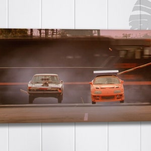 May include: A white Dodge Charger and an orange Toyota Supra race down a street. The Charger is in the foreground, while the Supra is in the air, having just jumped over a wooden plank. The background is blurred, suggesting speed.