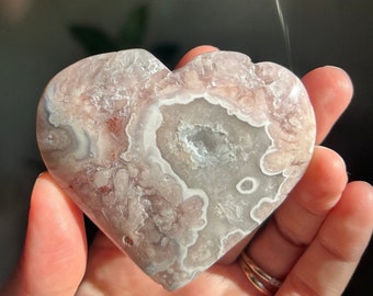 May include: A heart-shaped agate crystal with pink and white banding. The crystal has a natural, rough texture and a smooth, polished surface.