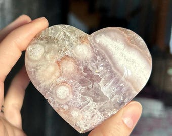 May include: A heart-shaped crystal with a pink and white agate pattern. The crystal has a smooth, polished surface and is translucent.
