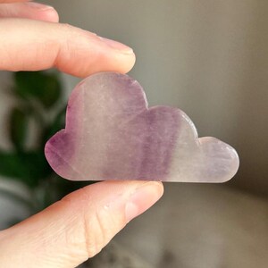 May include: A purple and white cloud-shaped fluorite crystal. The crystal is smooth and polished.