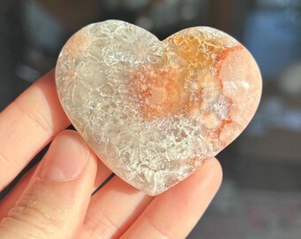 May include: A heart-shaped crystal with a white and orange color pattern. The crystal has a rough, textured surface.