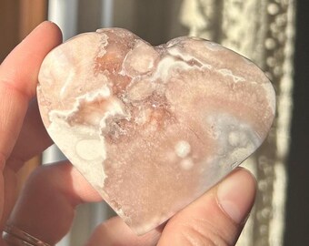 May include: A heart-shaped pink and white agate crystal with a smooth, polished surface. The crystal has a natural, organic pattern with swirls and white spots.