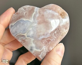 May include: A heart-shaped pink and white agate crystal with a polished surface. The crystal has a natural, organic shape and a swirling pattern of white and pink.