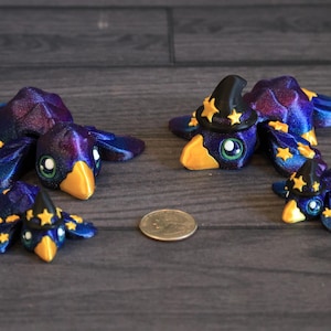 May include: Four whimsical, fantasy-themed crow figurines. The crows are primarily dark blue with iridescent purple accents, yellow beaks, and green eyes. One crow wears a black witch hat with yellow stars. A US quarter is included for size comparison.