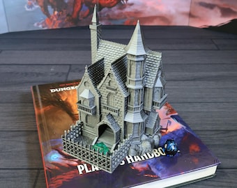 May include: A detailed gray miniature castle with multiple turrets and a fence, resting on a "Dungeons & Dragons" handbook. A blue and black die is next to the castle. The castle has a detailed facade and a textured roof.