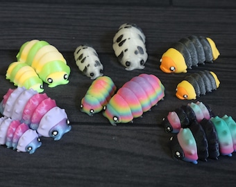 May include: A collection of twelve small, segmented pill bug figurines in various colour patterns, including rainbow gradients, yellow and green stripes, black and orange, white with black spots, and pink and blue ombre, all featuring large black eyes.