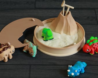 May include: A set of five small dinosaur figurines, including a green, red, blue, and two brown dinosaurs. The dinosaurs are arranged on a brown sand tray with a small volcano in the center.