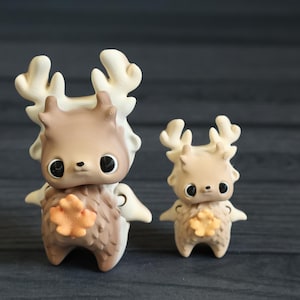 May include: Two small, brown and white deer figurines with orange accents. The larger deer has wings and the smaller deer has a leaf-shaped accent on its chest.