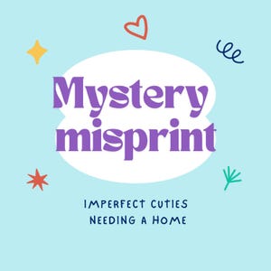 May include: A light blue background with a white cloud shape containing the text "Mystery misprint" in purple. The text "IMPERFECT CUTIES NEEDING A HOME" is below the cloud. There are various colorful shapes around the cloud, including a heart, stars, and a squiggly line.
