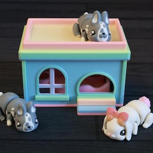 May include: Three gray and white bunny figurines with black eyes and pink noses. The bunnies are sitting on a pastel blue and pink toy house with a rainbow roof.