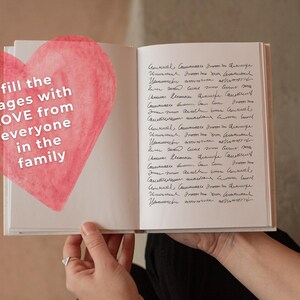 May include: A white journal with a pink watercolor heart on the front cover. The heart has the text "fill the pages with LOVE from everyone in the family" written on it. The journal is open to a page with handwritten text.