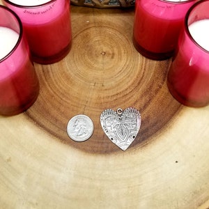May include: Four pink glass candle jars with white wax and a silver heart-shaped pendant on a wooden surface.