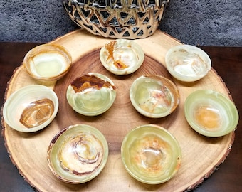 May include: Nine small, green, brown, and white onyx bowls arranged in a circle on a wooden platter. The bowls are all different shapes and sizes, and they have a natural, organic look.