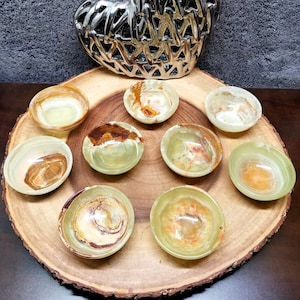 May include: Nine small, green, brown, and white onyx bowls arranged in a circle on a wooden platter. The bowls are all different shapes and sizes, and they have a natural, organic look.