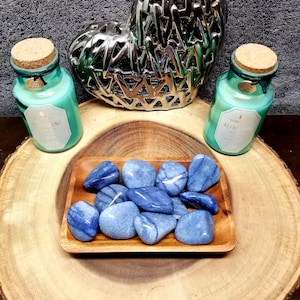 May include: A wooden bowl filled with blue and white agate tumbled stones. The bowl is sitting on a wooden surface. There are two glass bottles with cork tops and labels that say "Live your dream" and "Refreshing" on the left and "Aroma Refreshing" on the right.