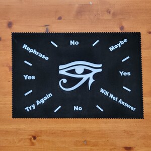 May include: Black felt Ouija board with a white eye symbol and the words "Rephrase", "Yes", "Try Again", "No", "No", "Maybe", "Yes", "Will Not Answer" around the edge.