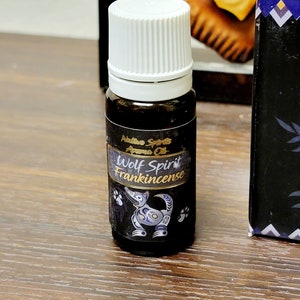 May include: A small brown glass bottle with a white cap. The label is black with gold lettering and a wolf design. The label reads "Native Spirits Aroma Oil Wolf Spirit Frankincense".