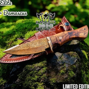 Puede incluir: Un cuchillo de cobre de Damasco con mango de madera y funda de cuero. La hoja tiene un patr&oacute;n intrincado. El cuchillo est&aacute; etiquetado como "Elite Copper Damascus" y "Limited Edition". La funda es marr&oacute;n.