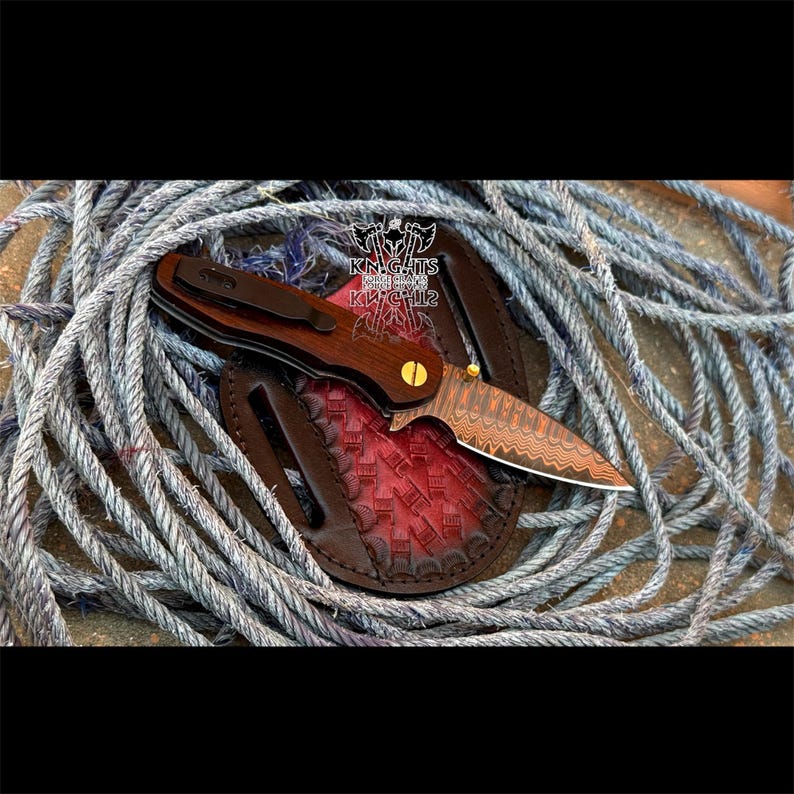 May include: A folding pocket knife with a dark wood handle, a black metal pocket clip, and a patterned blade featuring a wavy design. The knife rests on a circular, embossed red leather sheath with the text KNIGHTS printed in white.
