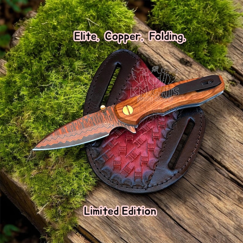 May include: A folding knife with a patterned copper blade and a wood handle, featuring a black pocket clip and a brass pivot screw. The knife rests on a circular, embossed red and black leather sheath. Text reads: Elite, Copper, Folding, Limited Edition.
