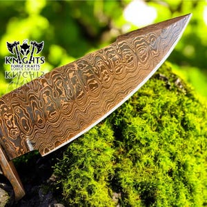 Puede incluir: Primer plano de una hoja de cuchillo de acero de Damasco con un patr&oacute;n &uacute;nico. La hoja es marr&oacute;n y plateada, con un mango de madera. El cuchillo descansa sobre musgo verde. El logotipo "KNIGHTS FORGE CRAFTS" es visible.