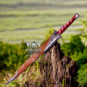 May include: A decorative dagger with a red and silver handle and a brown sheath. The blade is partially visible, and the dagger rests on a tree stump. The handle has a red and white pattern. The dagger is a medieval-themed item.
