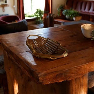 Puede incluir: Una mesa de madera con un acabado natural y una cesta tejida de materiales naturales. La mesa tiene un aspecto rústico y está hecha de madera maciza. La cesta es de estilo tradicional y es perfecta para guardar fruta u otros objetos.