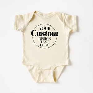 May include: A cream-colored baby onesie with a black circle containing the text "YOUR Custom DESIGN TEXT LOGO".
