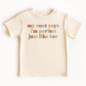 May include: A cream colored short-sleeved t-shirt with the text "my aunt says i'm perfect just like her" in colorful letters.