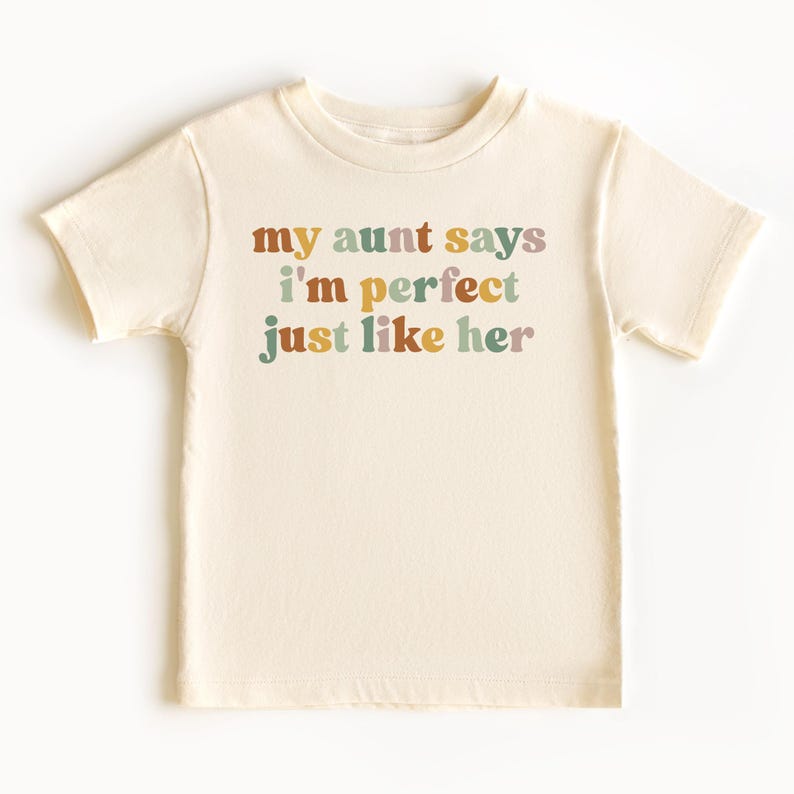 May include: A cream colored short-sleeved t-shirt with the text "my aunt says i'm perfect just like her" in colorful letters.