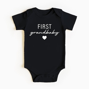 May include: Black baby onesie with white text that reads "FIRST grandbaby" with a small white heart.