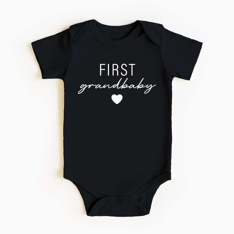 May include: Black baby onesie with white text that reads "FIRST grandbaby" with a small white heart.