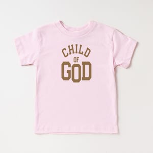 May include: Pink toddler t-shirt with brown text that reads "CHILD OF GOD" in a varsity style font.