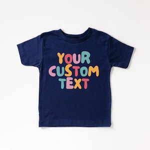 May include: A navy blue t-shirt with the text "YOUR CUSTOM TEXT" in colorful, bubble-like letters.