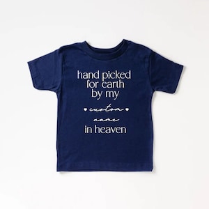 以下が含まれることがあります： 白文字で「hand picked for earth by my custom name in heaven」と書かれた、紺色の半袖Tシャツです。