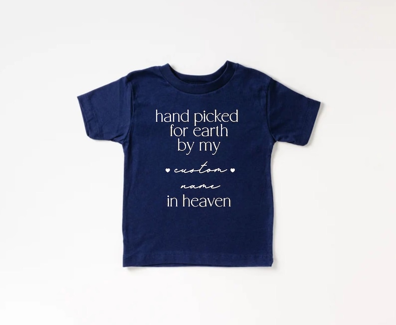 以下が含まれることがあります： 白文字で「hand picked for earth by my custom name in heaven」と書かれた、紺色の半袖Tシャツです。