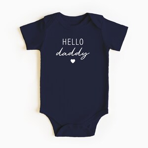 May include: A navy blue baby onesie with white text that reads "HELLO daddy" and a small white heart.
