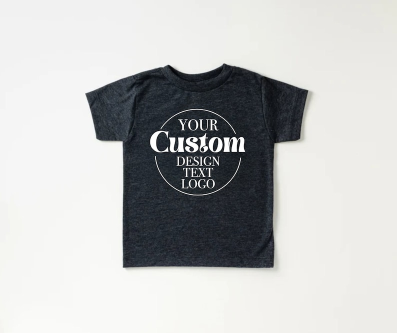 Op de afbeelding: Een donkergrijs T-shirt met een witte cirkel op de voorkant met de tekst "YOUR Custom DESIGN TEXT LOGO".