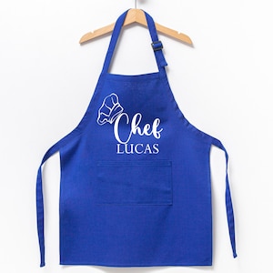 K&ouml;nnte beinhalten: Blaue Kochsch&uuml;rze mit einer wei&szlig;en Kochm&uuml;tze und dem Text "Chef Lucas" auf der Vorderseite.